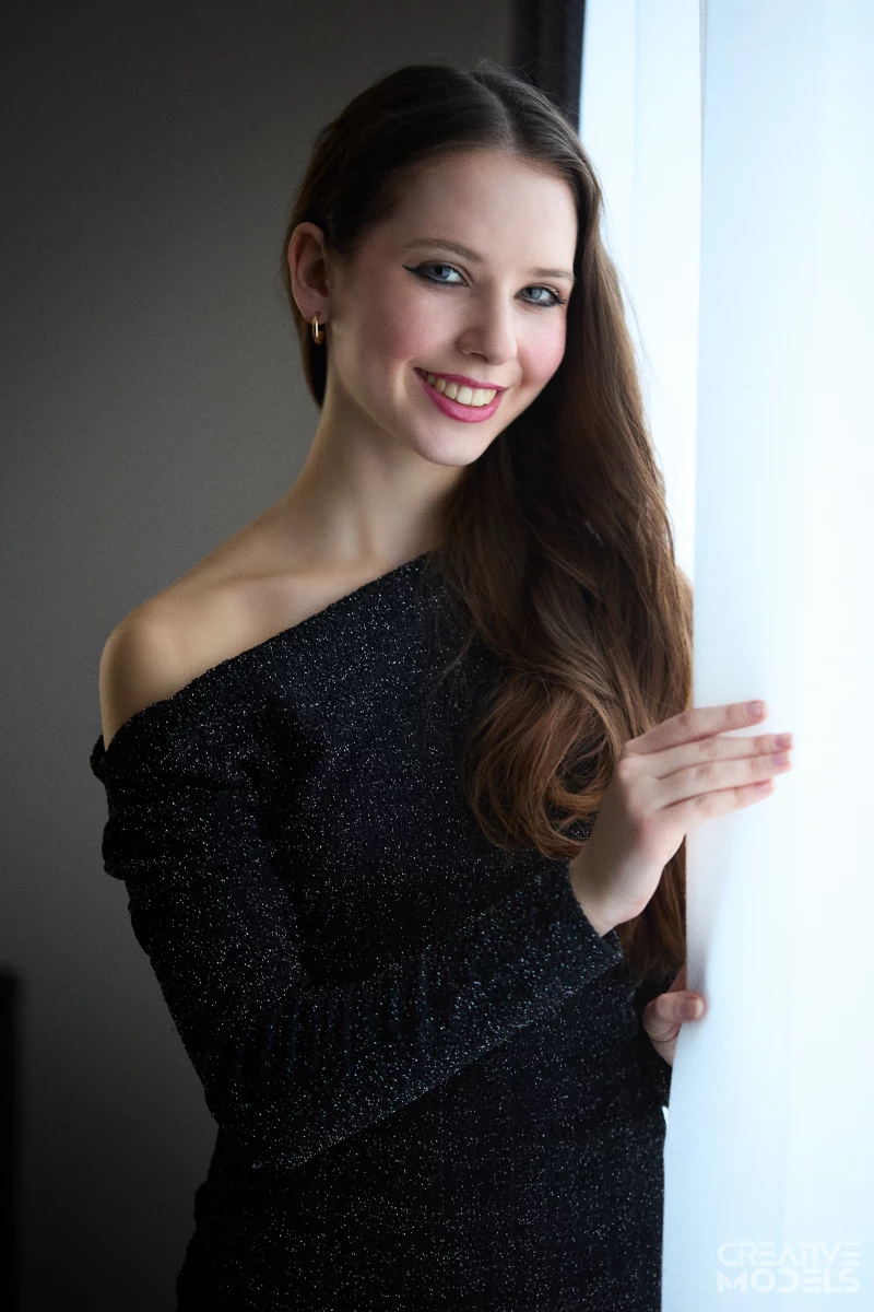Model Juliette vor dem Fenster mit Vorhang im sonnigen Schein.